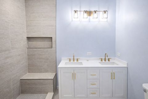 Bathroom with a double white vanity, brass fixtures, and tiled shower seating