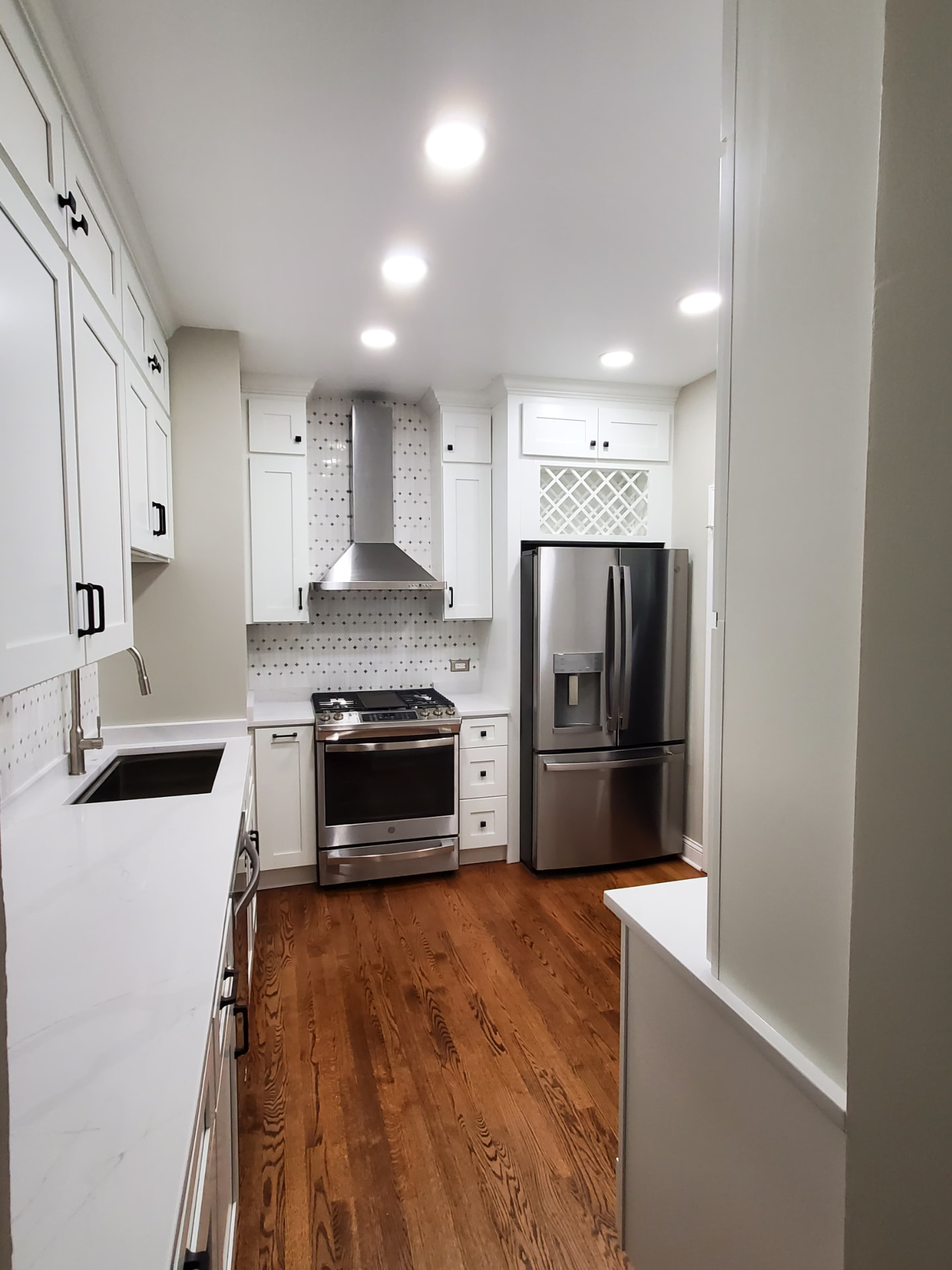 L-shaped kitchen with white shaker cabinets, white quartz countertops, diamond-tile backsplash, and hardwood floor